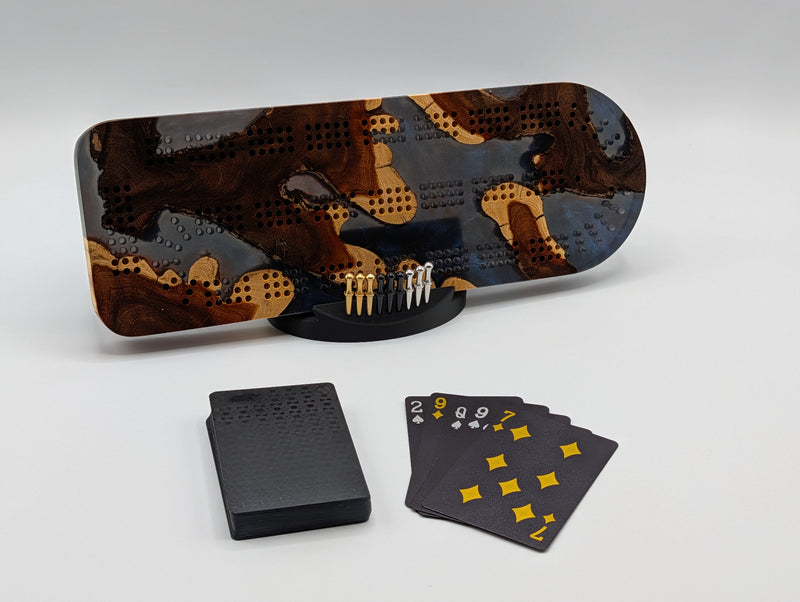 Midnight Islands Origin brasiletta cribbage board with smoky midnight blue resin — shown with included cards, pegs and display stand.