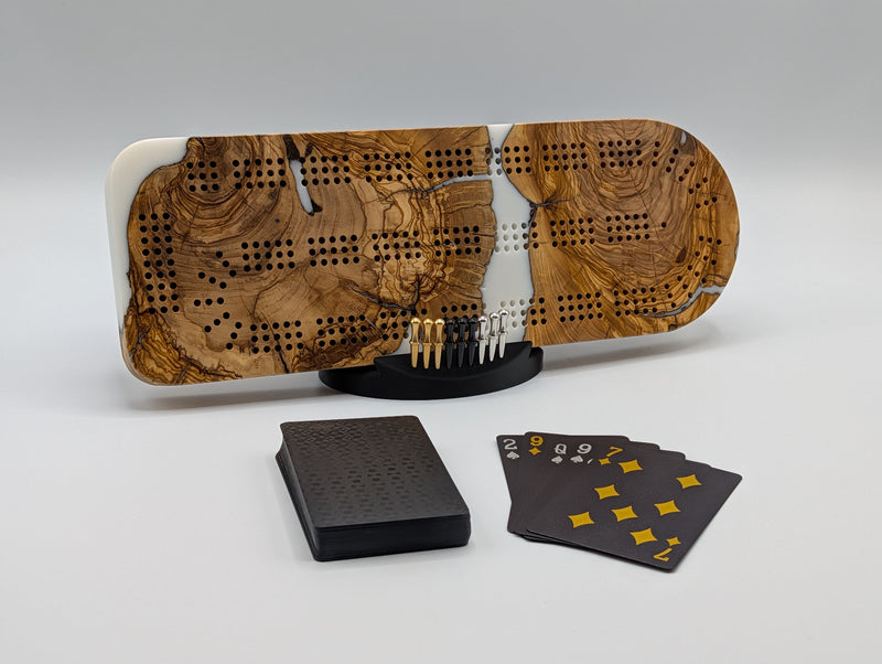 Ivory Crossing Origin Turkish olivewood cribbage board with white resin — shown with included cards, pegs and display stand.