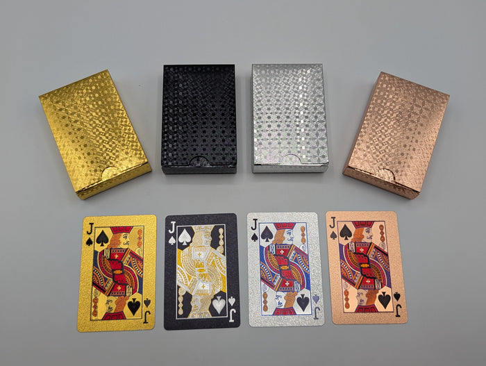 Four waterproof playing-card decks in gold, black, silver and rose gold, with matching foil-finished cards shown beneath the boxes.