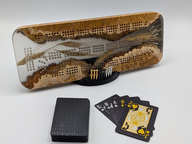 One-of-a-kind Imprint brown mallee burl cribbage board with real Saskatchewan-grown wheat, on its included display stand with pegs and a black playing-card deck.