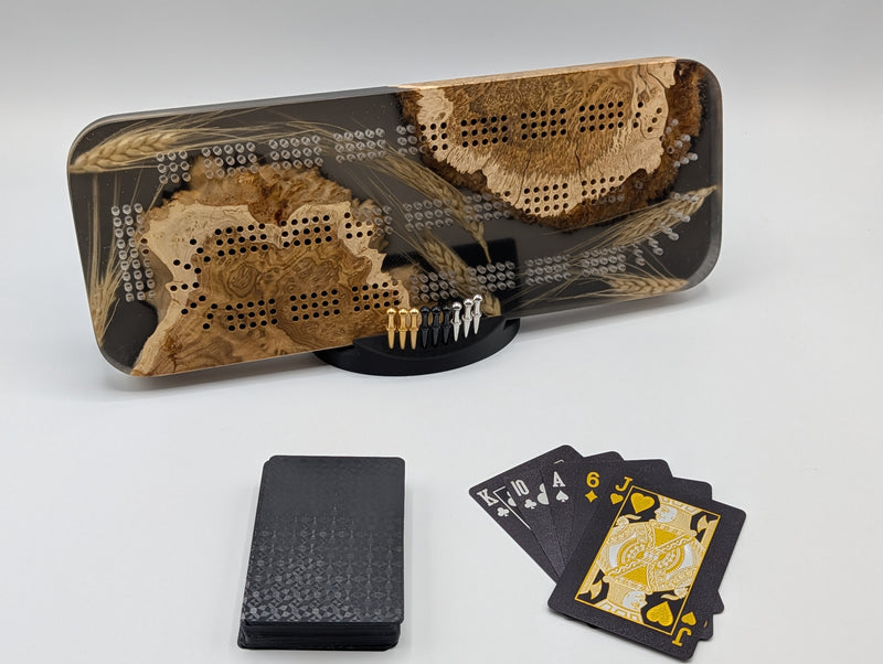 One-of-a-kind Imprint brown mallee burl cribbage board with real Saskatchewan-grown wheat, on its included display stand with pegs and a black playing-card deck.
